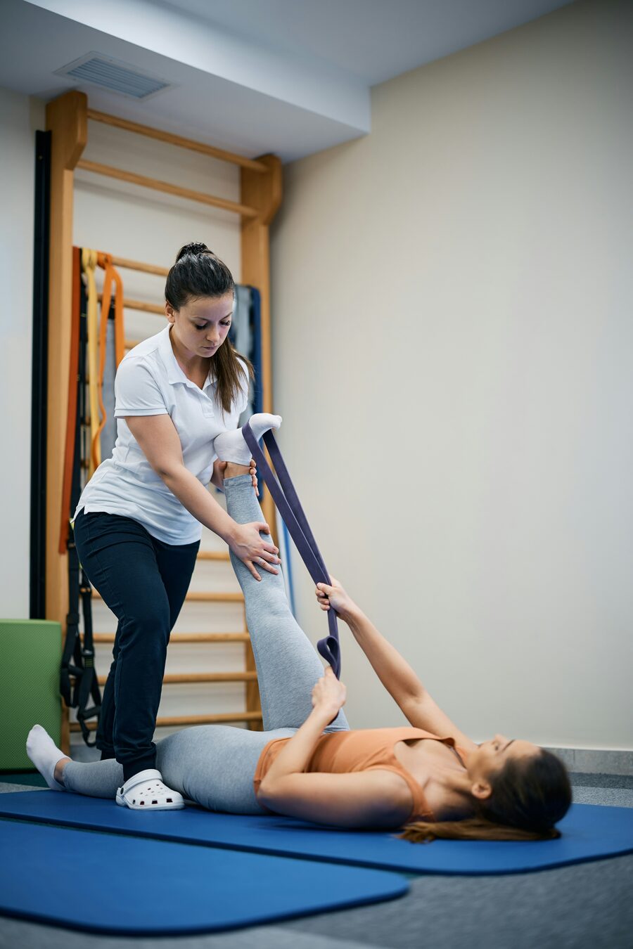 A physical therapist guiding a patient through a hamstring stretch with a band